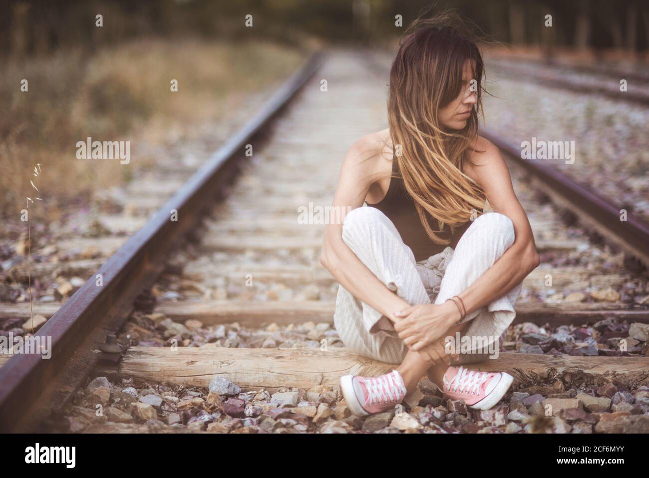 Donna dai capelli lunghi seduta sulle ferrovie in erba secca Foto Stock