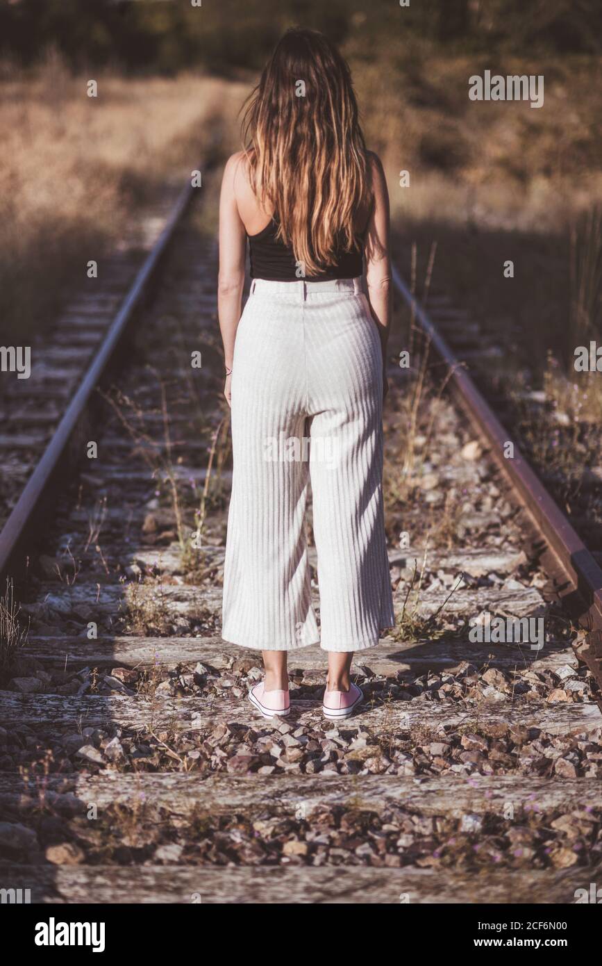 Donna dai capelli lunghi in piedi sulle ferrovie è cresciuta con erba secca Foto Stock