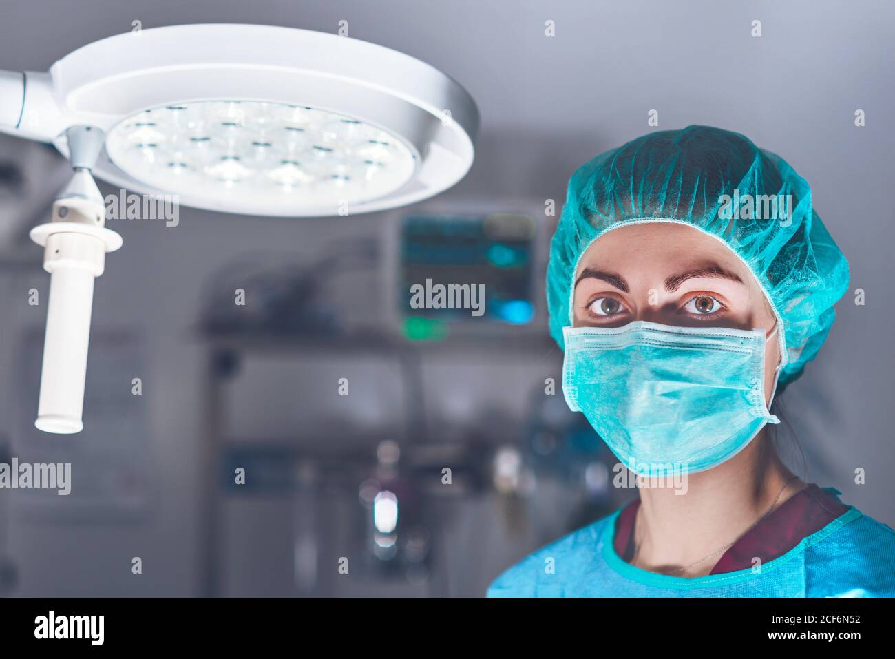 Donna adulta in maschera medica e cappello guardando la macchina fotografica prima di eseguire un intervento chirurgico in ospedale Foto Stock