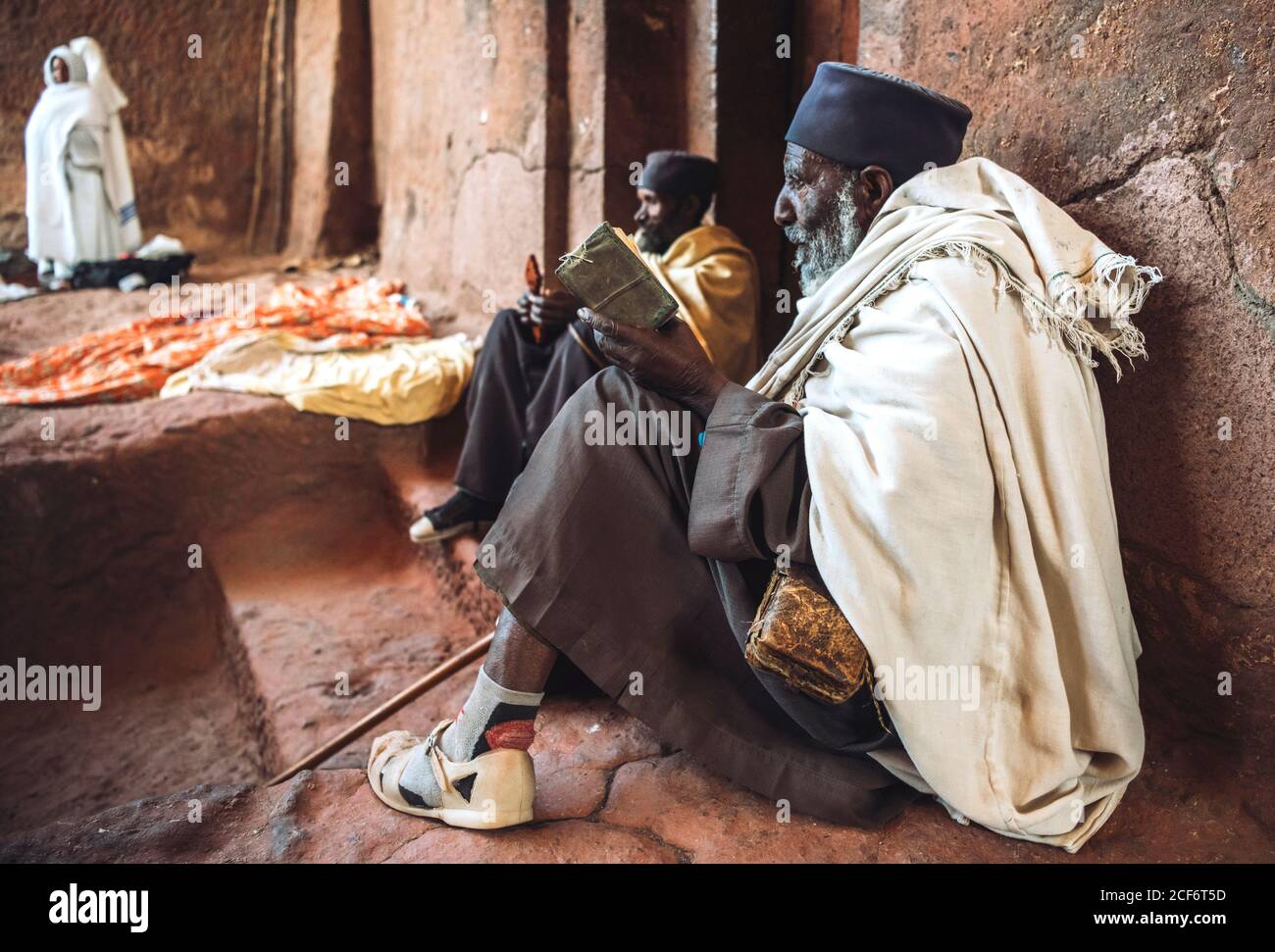 Lalibela, Etiopia - 04 novembre 2018: Vista laterale di anziani poveri preghiere in chiodi di garofano seduti accanto al muro di scabia in un'antica chiesa monolitica, Etiopia Foto Stock