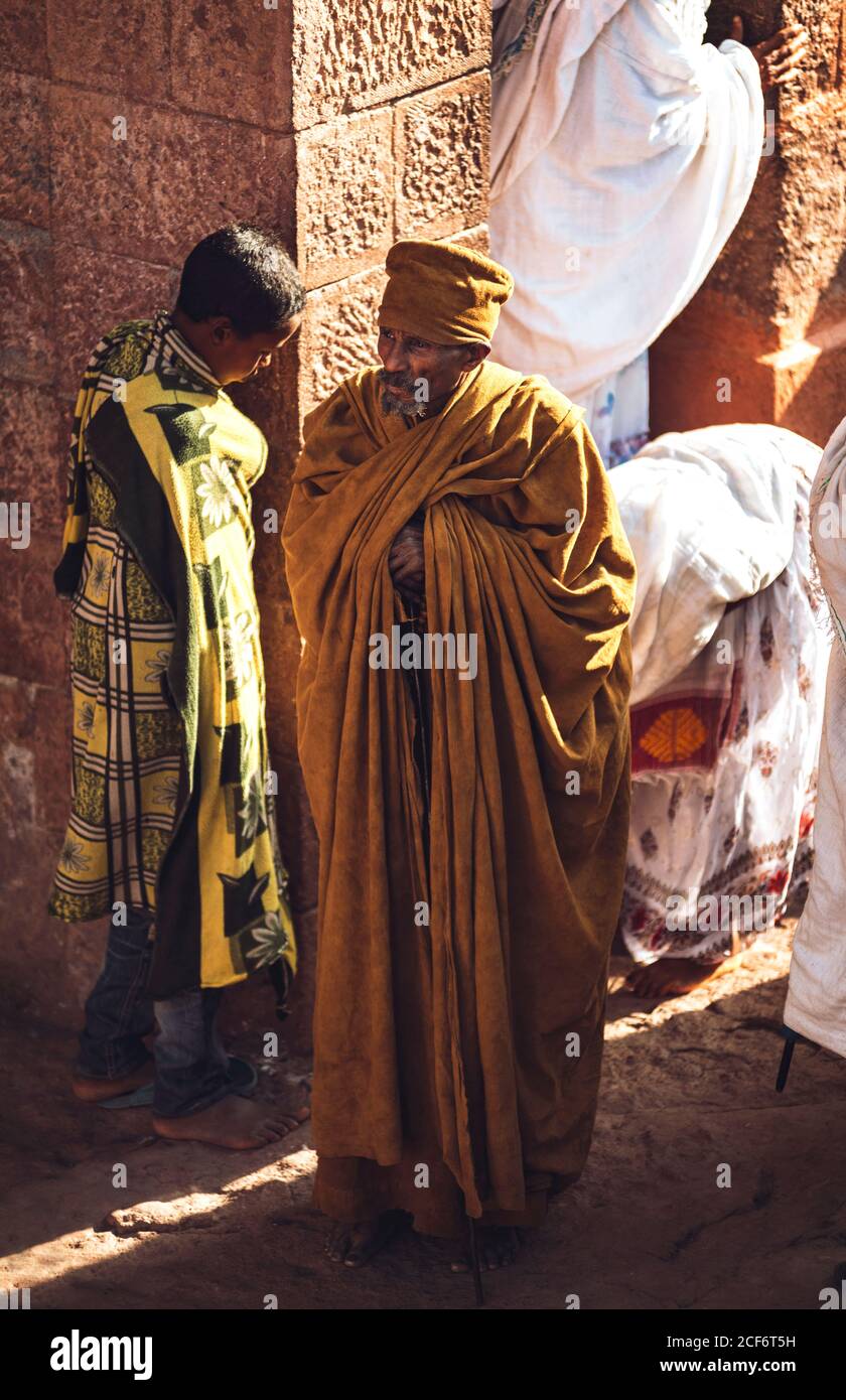 Lalibela, Etiopia - 04 novembre 2018: Anziano uomo etnico in abito lungo in piedi sulla roccia di antica chiesa monolitica con preghiere, Etiopia Foto Stock