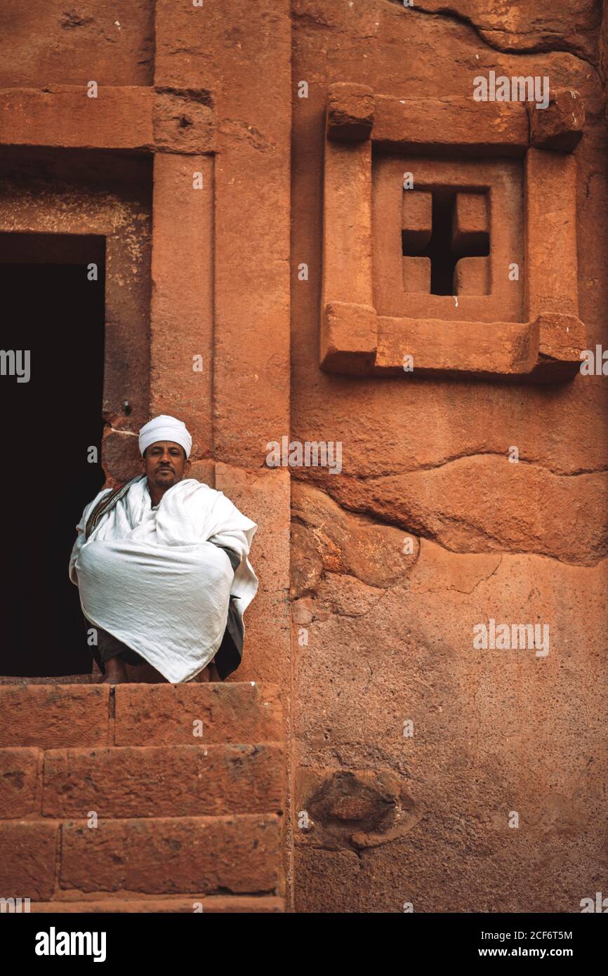 Lalibela, Etiopia - 04 novembre 2018: Sacerdote seduto sul portico della vecchia chiesa ortodossa scavata nella roccia a Lalibela, Etiopia Foto Stock