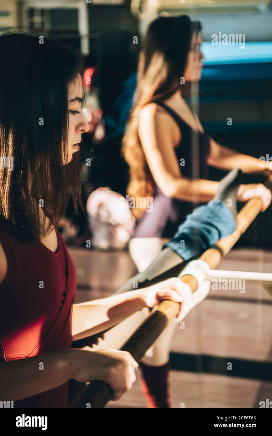 Giovani ballerine allenano in uno studio soleggiato in piedi vicino a specchio con barre. Foto Stock