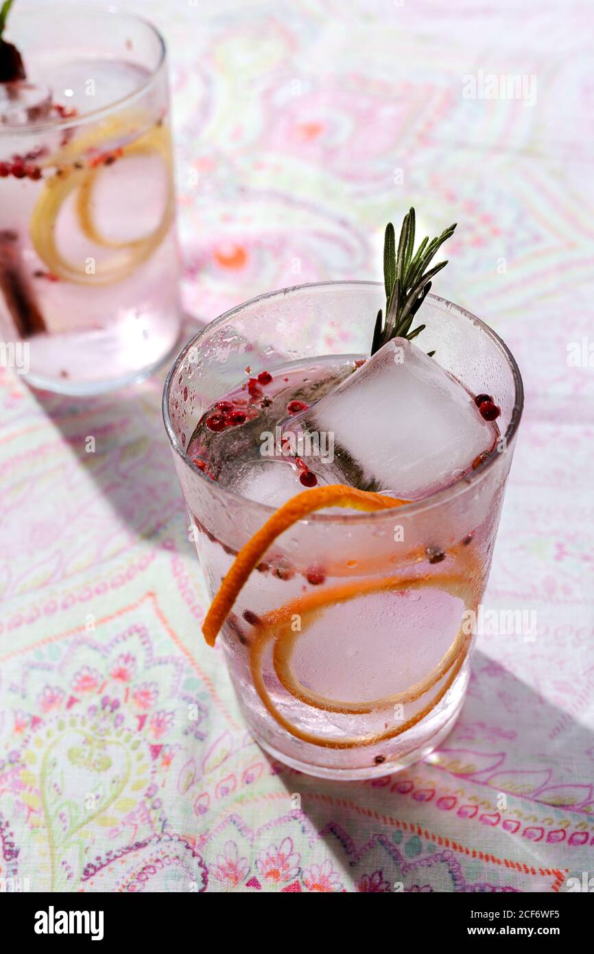 Cocktail tonico gin con acqua tonica rosa, pepe rosa, rosmarino, menta,  cannella, limone e arancia al sole su un tavolo da ristorante Foto stock -  Alamy