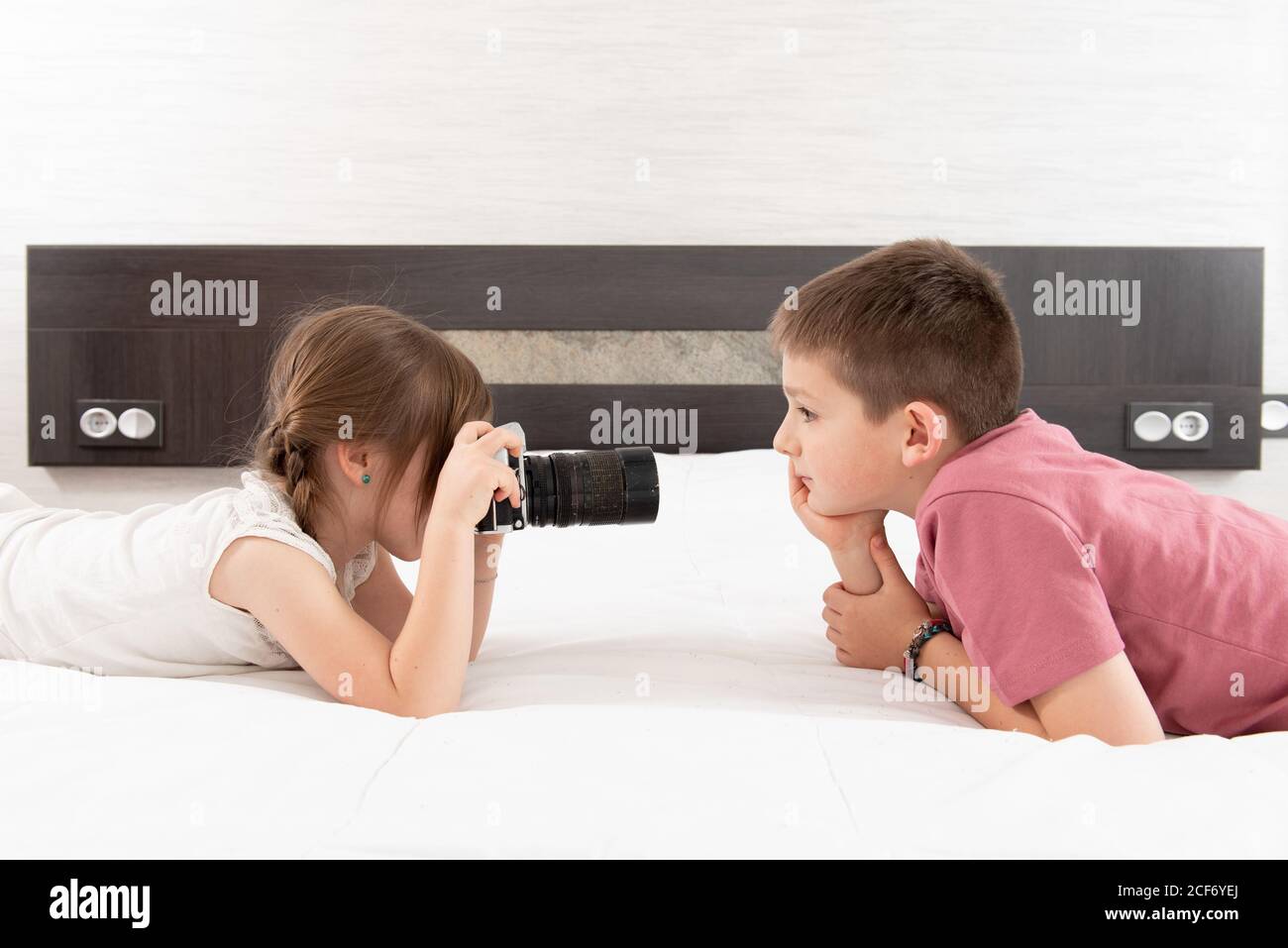 Vista laterale della bella sorella scattando foto di fratello sopra macchina fotografica mentre si è sdraiati a letto a casa Foto Stock