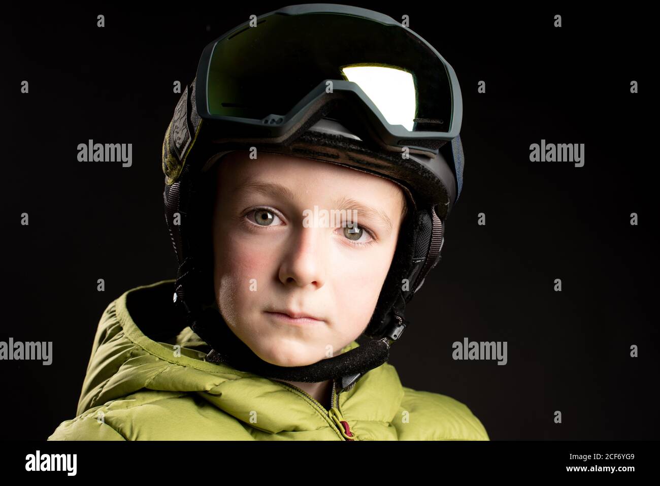 Piccolo capretto sportivo messo a fuoco in vestiti invernali con goggle di sci su sfondo nero in studio guardando la fotocamera Foto Stock