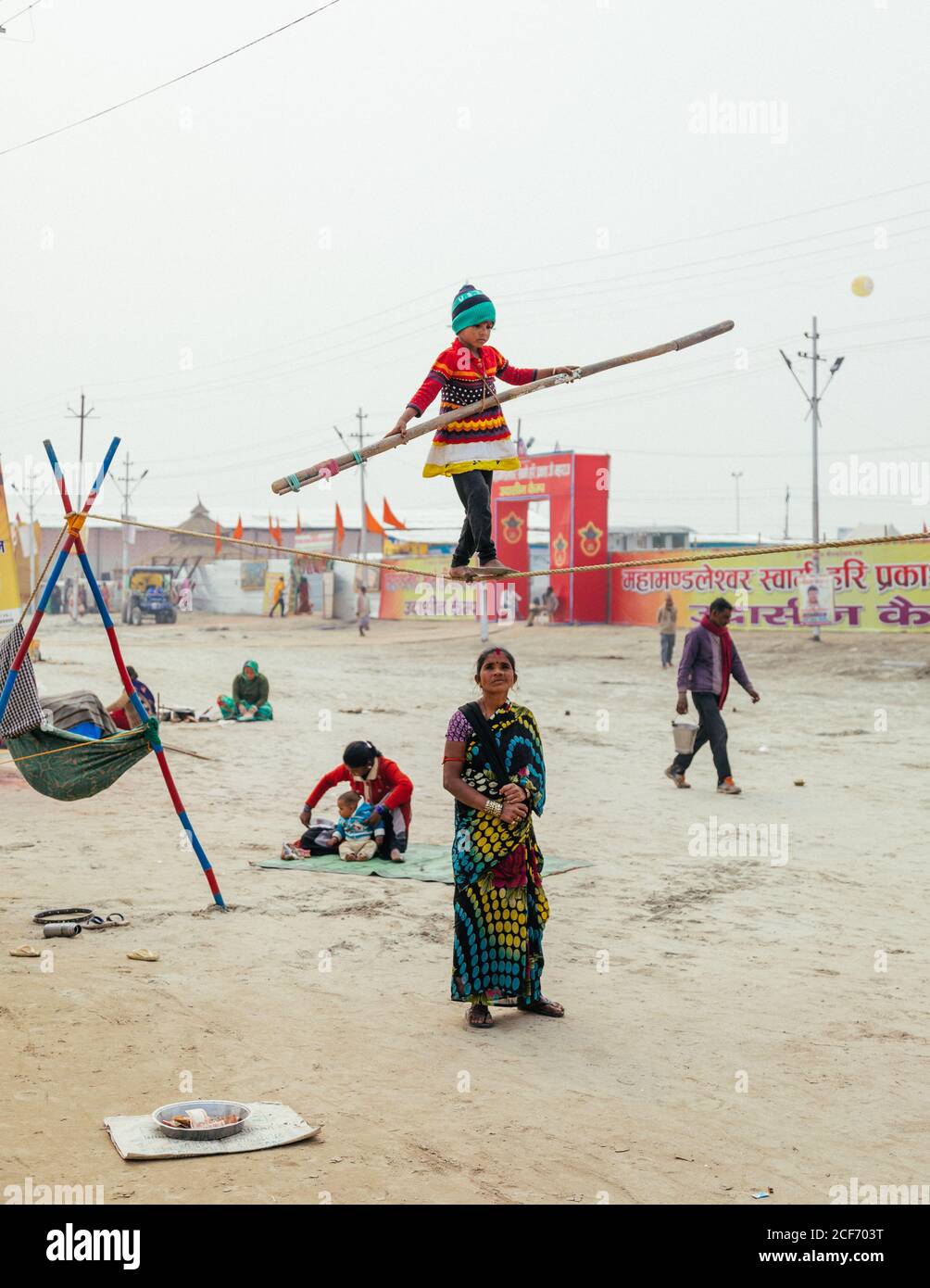 Allahabad, India - Febbraio, 2018:festeggiamenti in piazza dove il bambino tightrope camminano lungo la corda mentre la ragazza in sari guardando in su Foto Stock