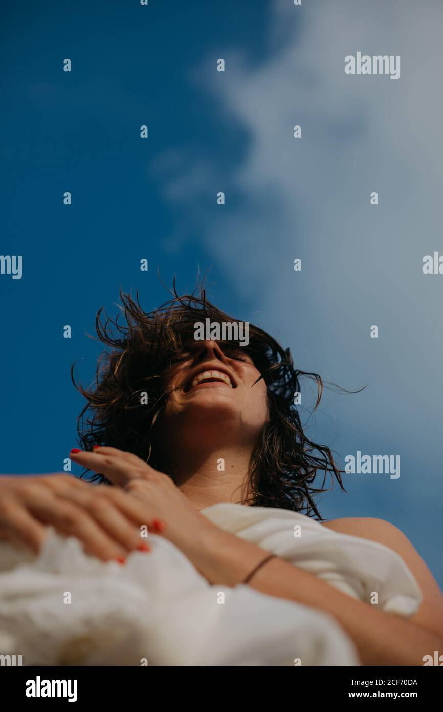 Da sotto di giovane donna allegra con capelli bagnati rilassarsi sulla spiaggia sabbiosa nella giornata di sole Foto Stock