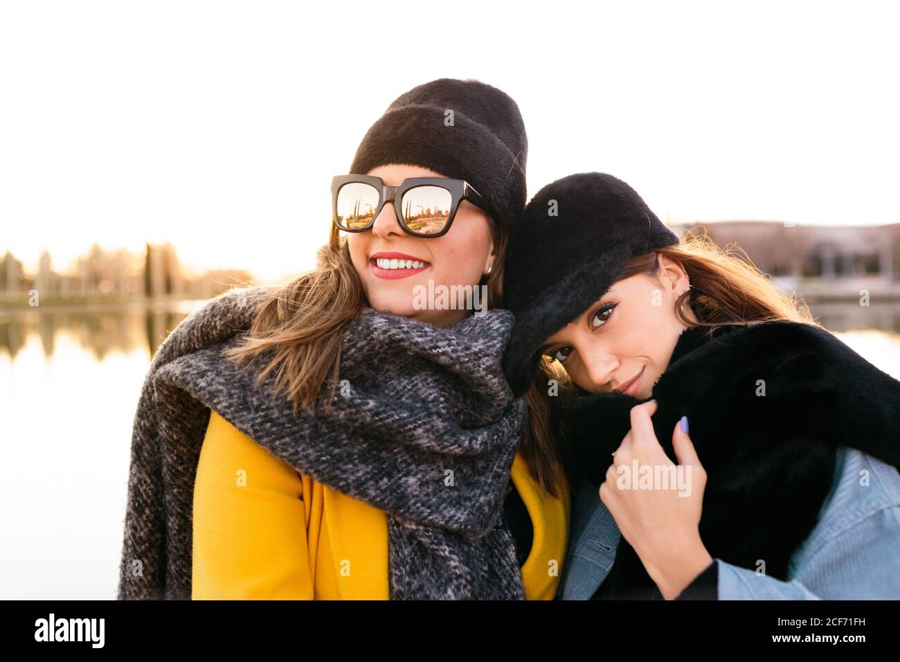 Donna soddisfatta in abiti caldi e occhiali da sole con un'amica elegante durante il viaggio sul lago al tramonto Foto Stock