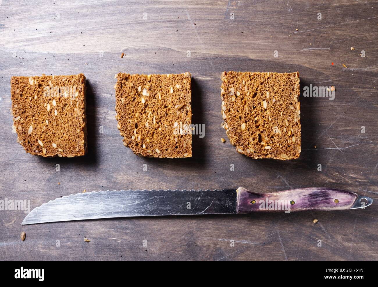 Vista dall'alto del pane marrone a fette con grani interi e. coltello da cucina su superficie di legno con briciole Foto Stock