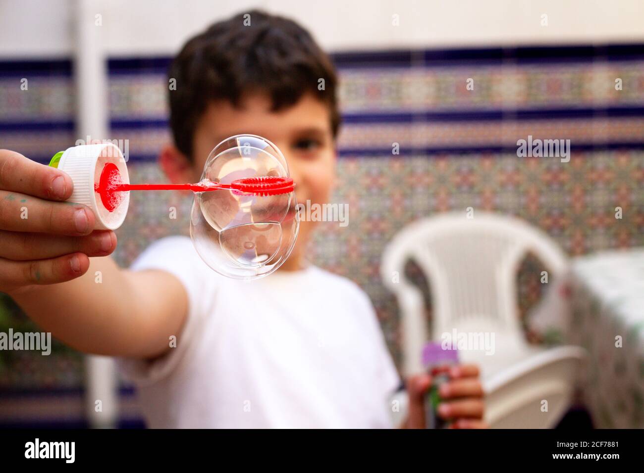 Bambino in T-shirt bianca che gioca bolle di sapone mentre si è in piedi sulla terrazza a casa Foto Stock