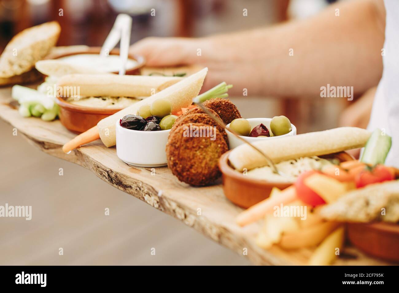 Crop anonima persona che tiene rustico vassoio di legno con vari tipi di antipasti durante la festa Foto Stock