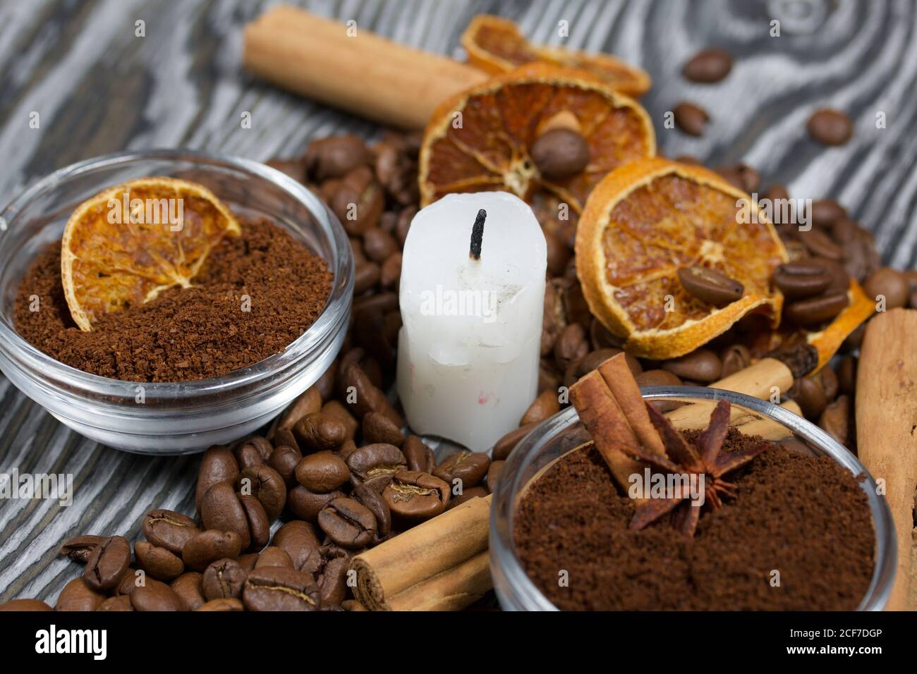 Chicchi di caffè su tela ruvida e stub di candela. Caffè macinato in contenitori e spezie. Su una superficie di tavole di pino spazzolato dipinte in bianco e nero. Foto Stock