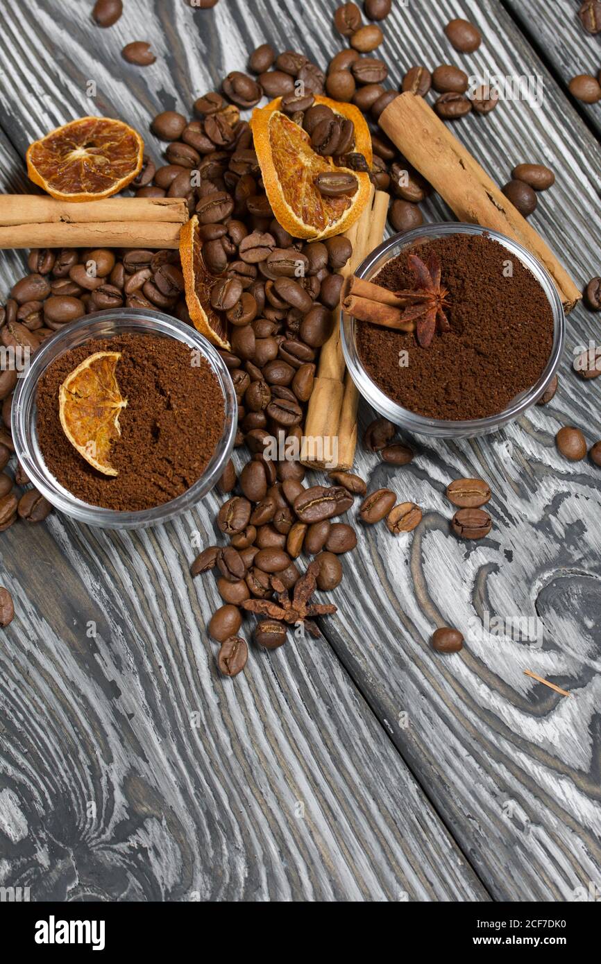 Chicchi di caffè. Caffè macinato in contenitori e spezie. Su una superficie di tavole di pino spazzolato dipinte in bianco e nero. Foto Stock