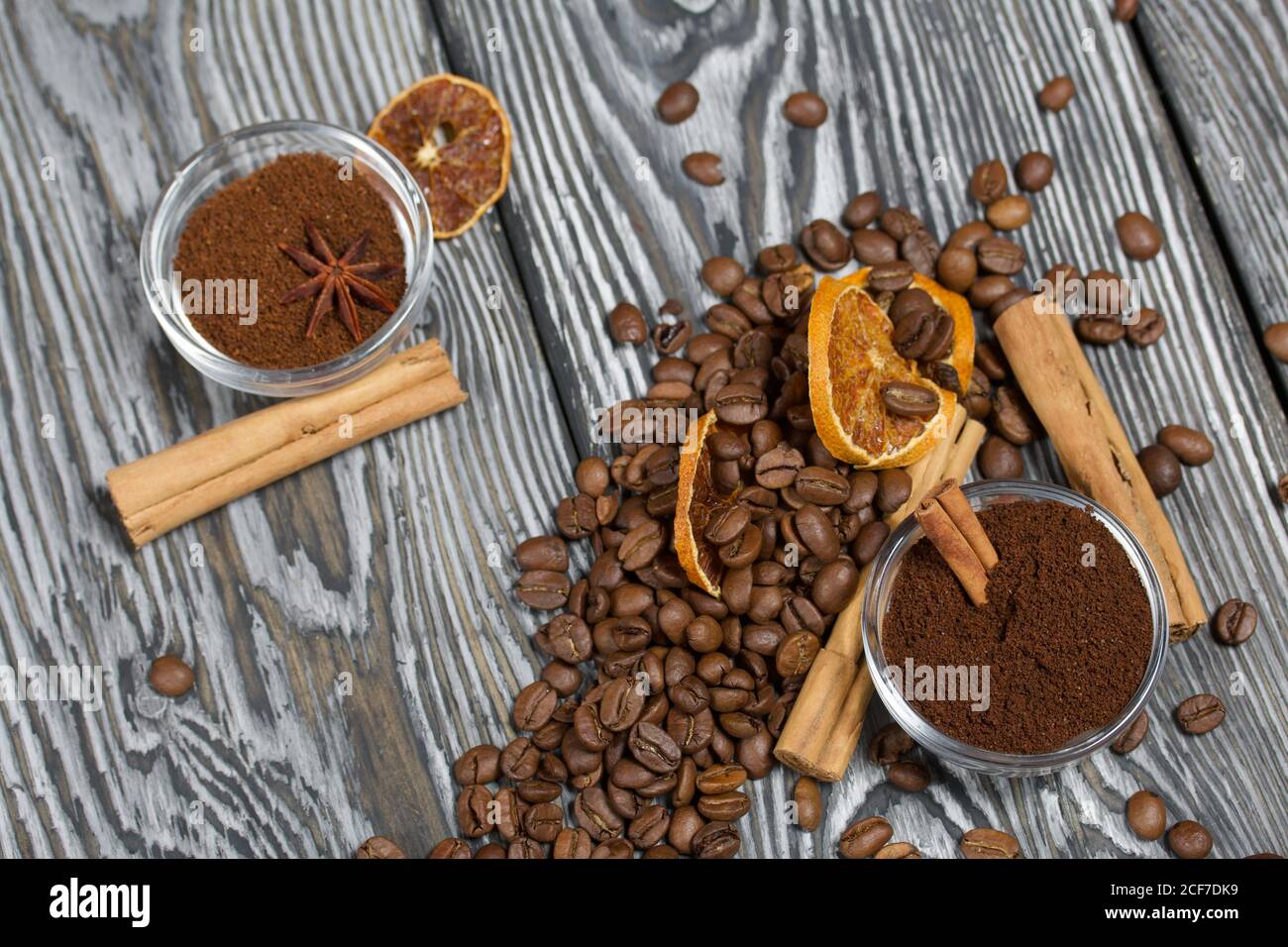 Chicchi di caffè. Caffè macinato in contenitori e spezie. Su una superficie di tavole di pino spazzolato dipinte in bianco e nero. Foto Stock