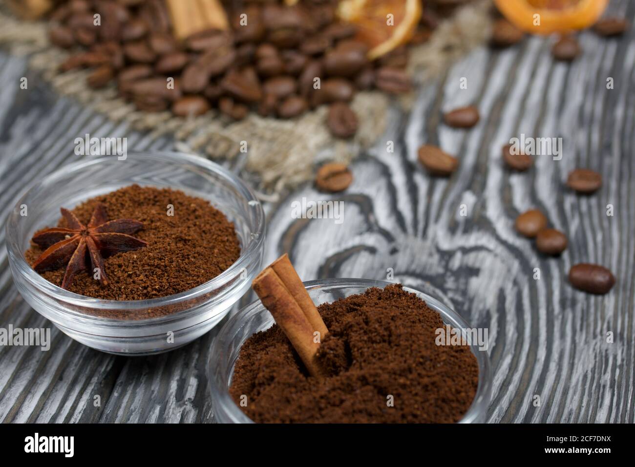 Chicchi di caffè su lino grosso. Caffè macinato in contenitori e spezie. Su una superficie di tavole di pino spazzolato dipinte in bianco e nero. Foto Stock