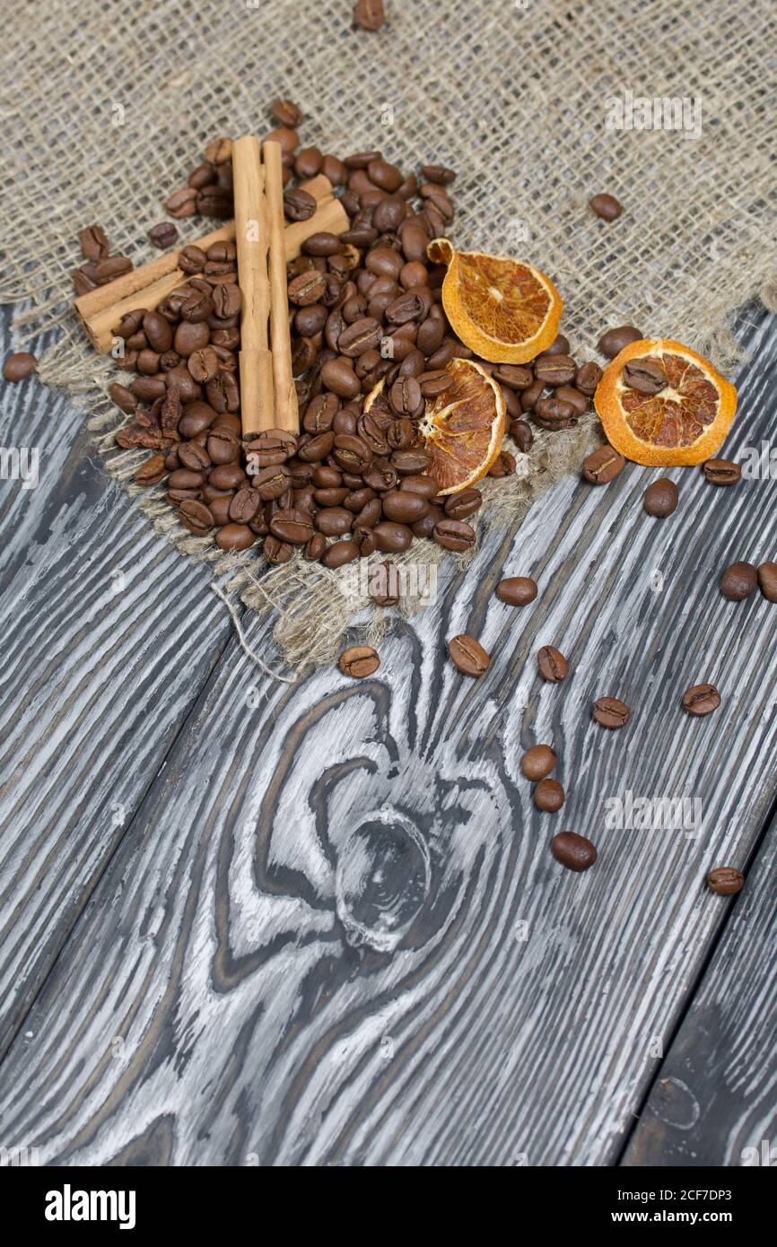 Chicchi di caffè su lino grosso e spezie. Su una superficie di tavole di pino spazzolato dipinte in bianco e nero. Foto Stock