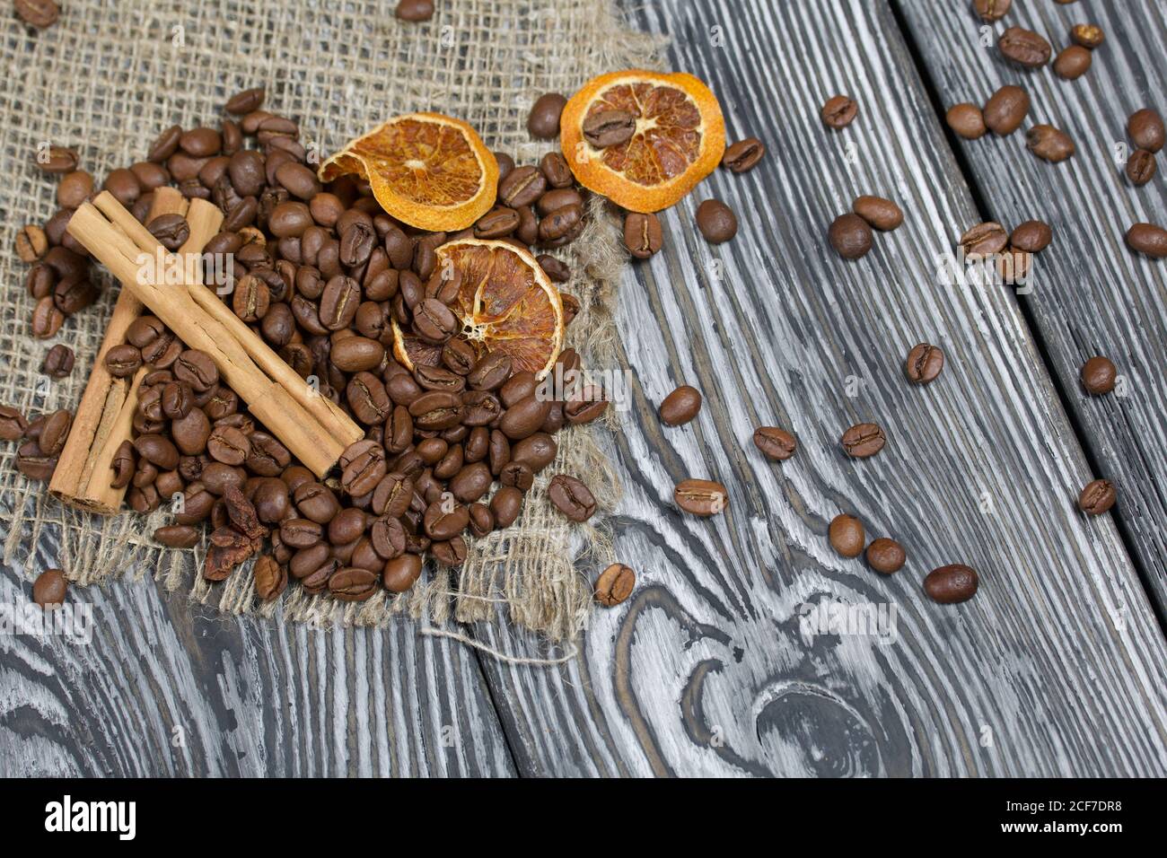 Chicchi di caffè su lino grosso e spezie. Su una superficie di tavole di pino spazzolato dipinte in bianco e nero. Foto Stock