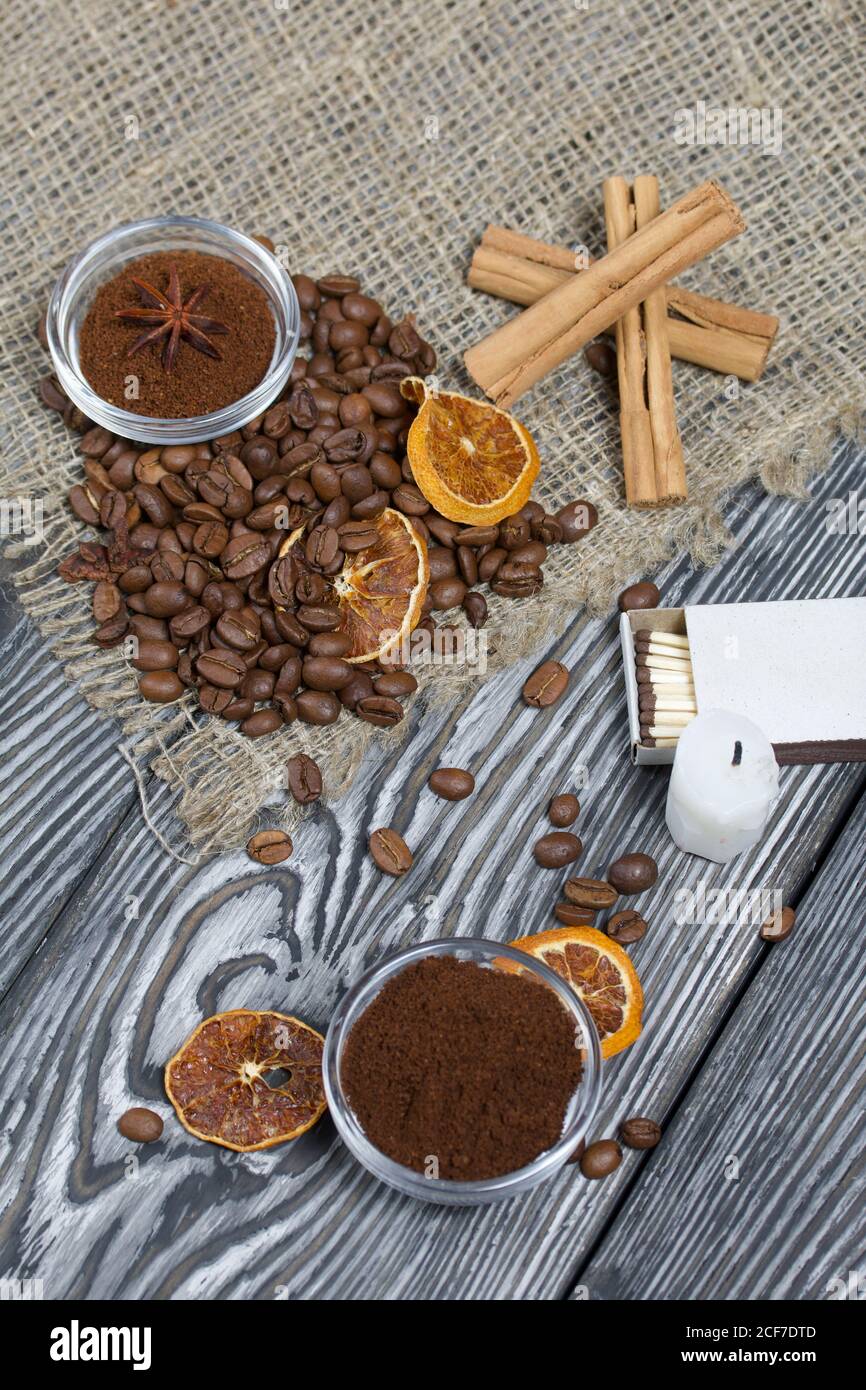 Chicchi di caffè su tela ruvida e stub di candela. Caffè macinato in contenitori e spezie. Su una superficie di tavole di pino spazzolato dipinte in bianco e nero. Foto Stock