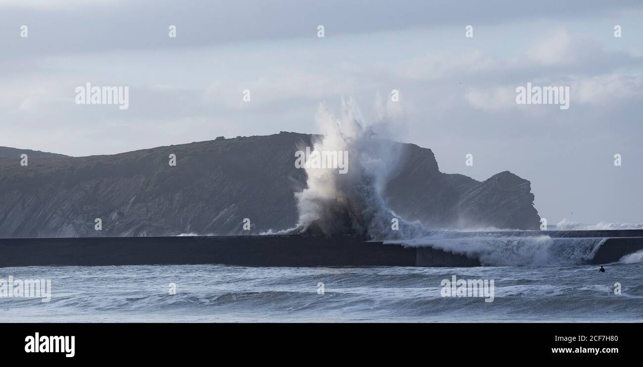 Le onde dell'oceano si infrangono sul molo con le alture come sfondo durante la marea Foto Stock