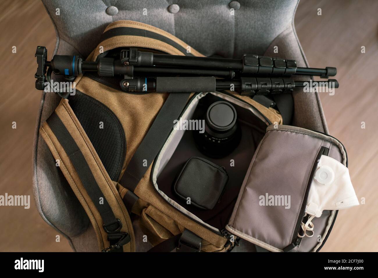 Vista dall'alto della borsa con moderni accessori fotografici e bianco maschera respiratore posizionata sulla sedia in camera Foto Stock