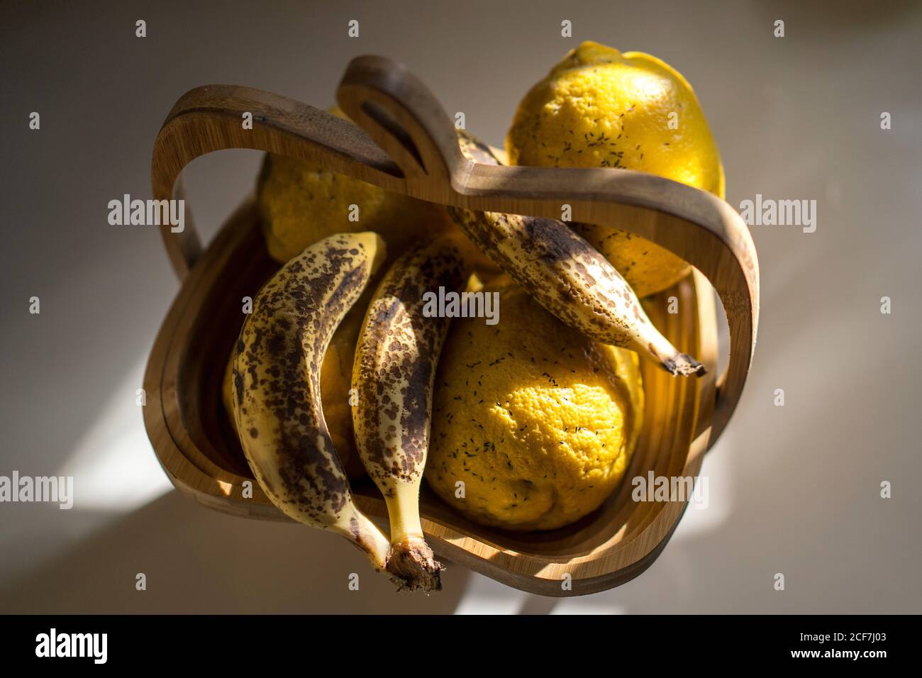 Dall'alto di banane fresche mature e limoni in legno cestino posto sul tavolo in cucina leggera Foto Stock