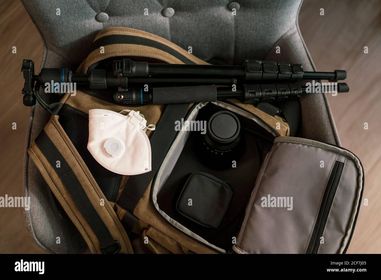Vista dall'alto della borsa con moderni accessori fotografici e bianco maschera respiratore posizionata sulla sedia in camera Foto Stock