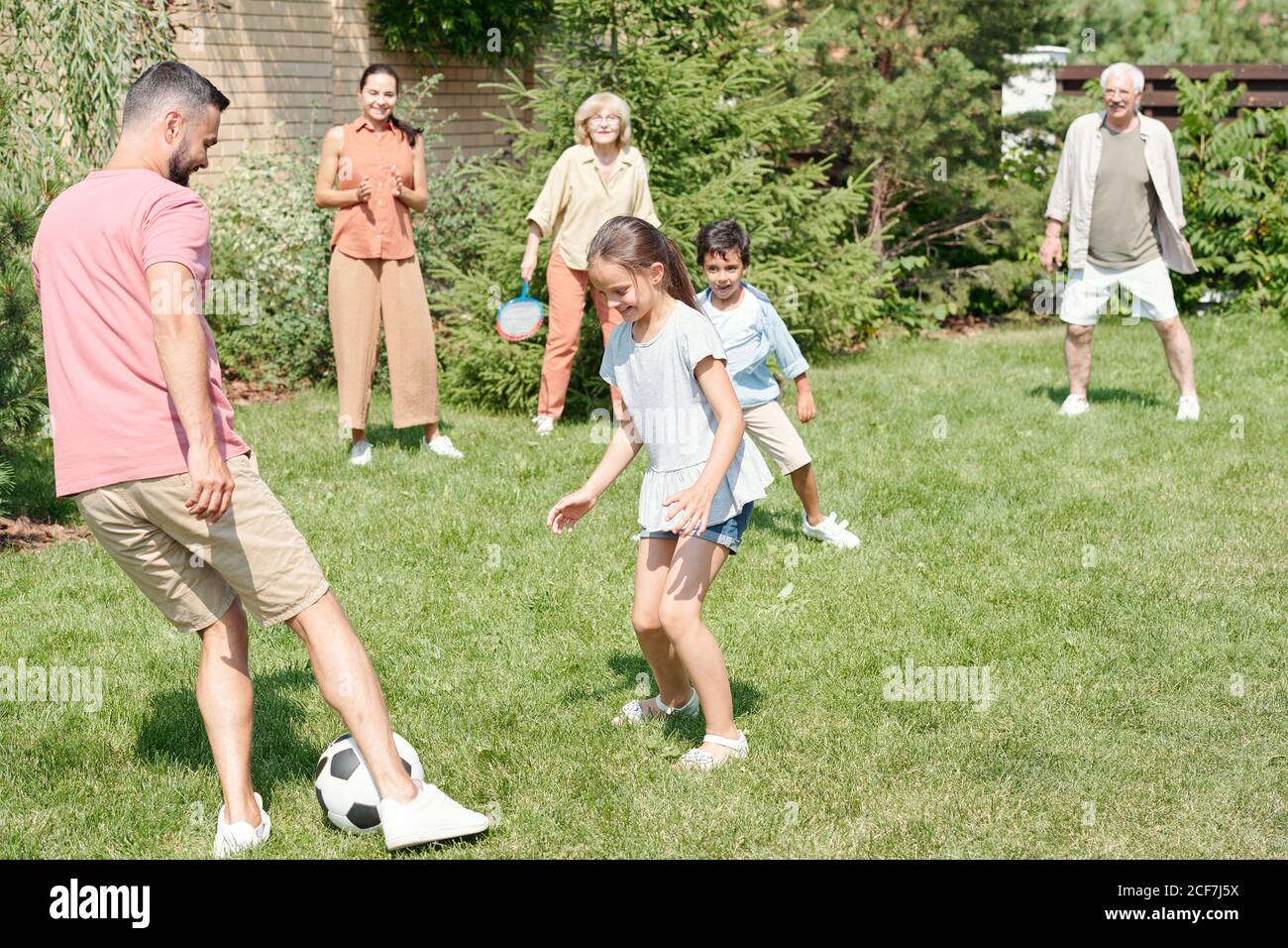 Nonno, papà e due bambini che giocano a calcio sul prato nel parco, nonna e mamma che li guardano Foto Stock