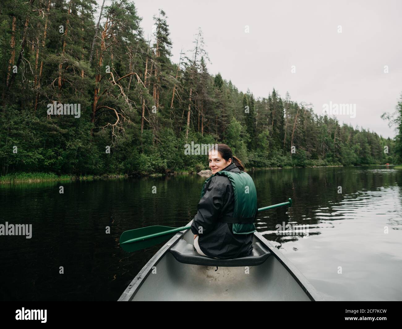 Giovane donna sorridente che guarda indietro mentre si va in barca sul fiume forestale in Finlandia Foto Stock