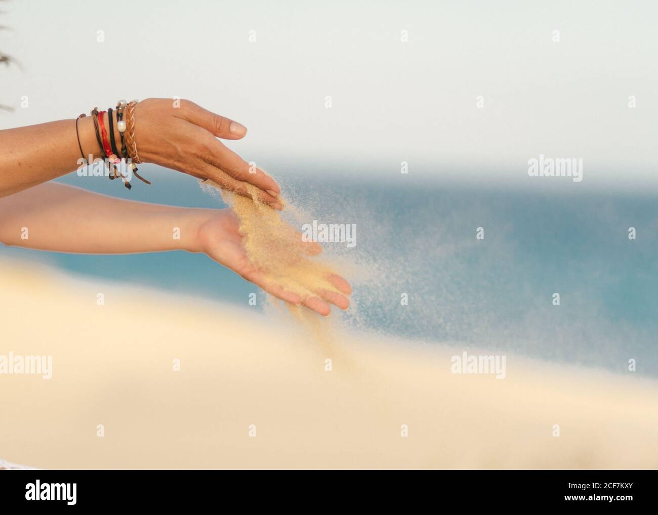Sabbia gialla pulita che vola dalle mani con bracciali luminosi di Crop Donna in spiaggia a Fuerteventura, Las Palmas, Spagna Foto Stock