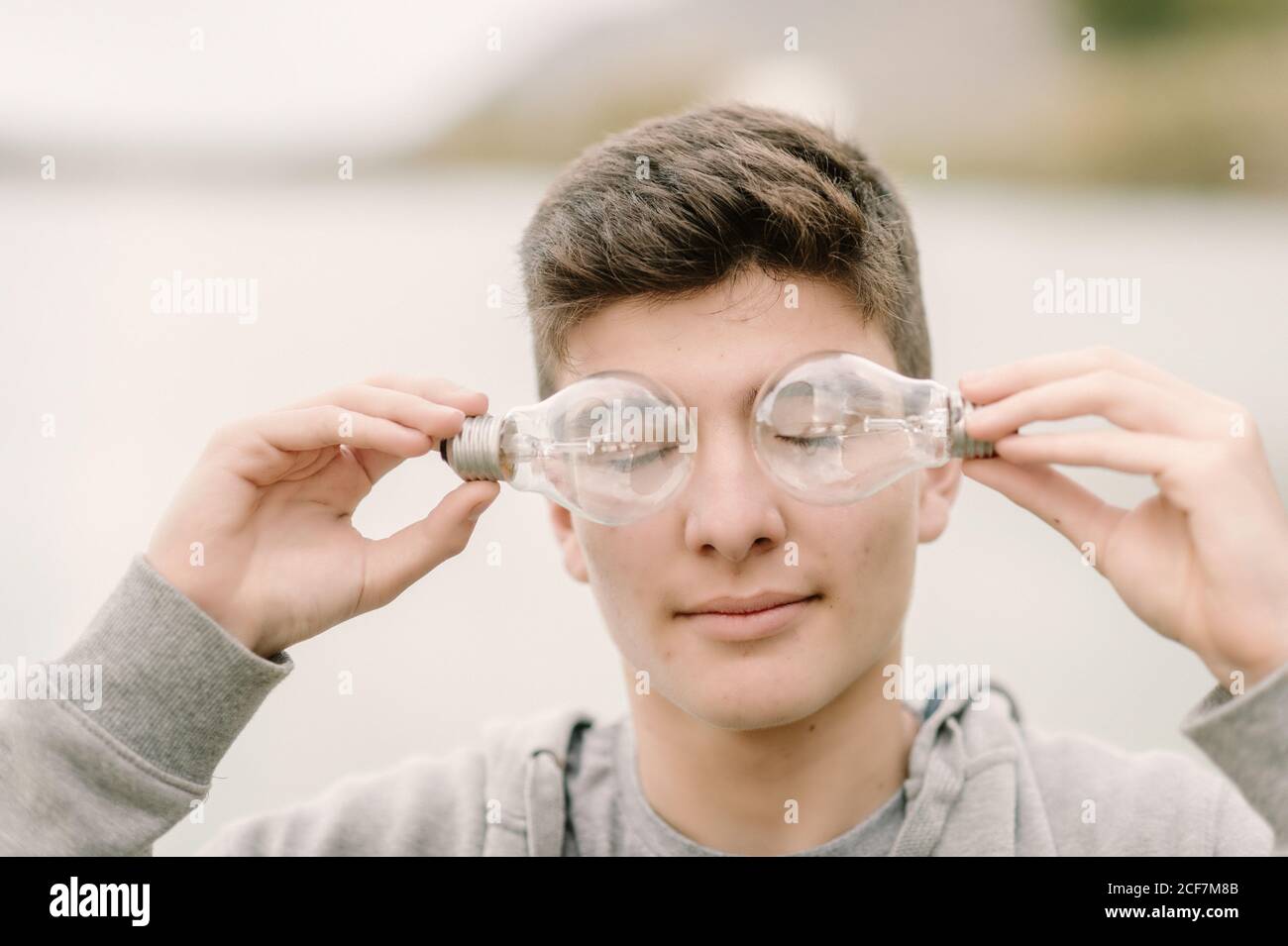 Ragazzo adolescente con un paio di lampadine davanti al suo concetto di innovazione e immaginazione a occhi chiusi Foto Stock