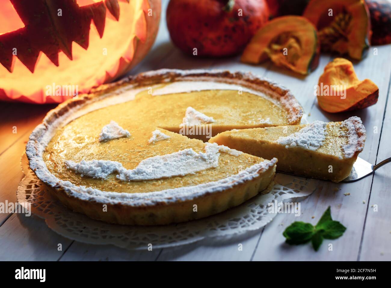 Deliziosa torta halloween di zucca fatta in casa con Jack-o-lanterna scolpita sullo sfondo. Torta d'arancia con menta e zucchero in polvere. Fotografia alimentare Foto Stock