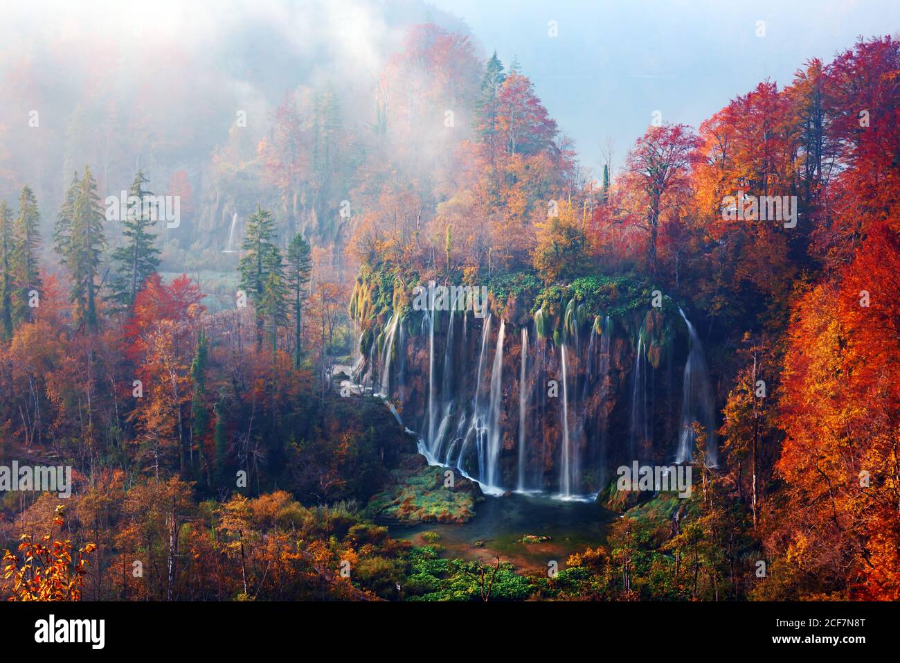 Incredibile vista sulla cascata delle nebbia nei laghi di Plitvice. Arancio autunno foresta sullo sfondo. Parco Nazionale di Plitvice, Croazia. Fotografia di paesaggio Foto Stock