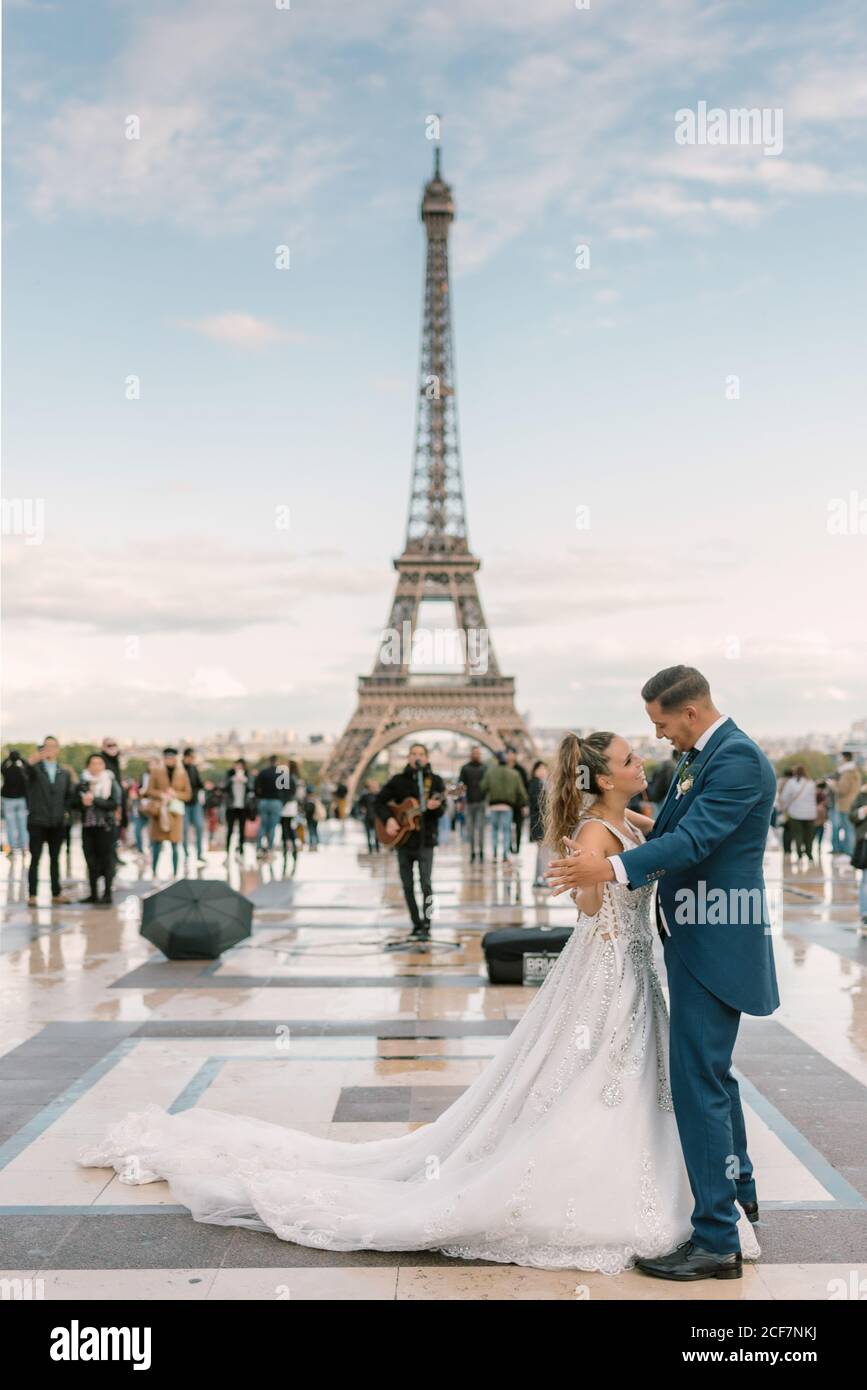 Sposo in abito da sposa blu in abito da sposa bianco avere danza lenta sorridente e guardarsi l'un l'altro con Torre Eiffel sullo sfondo a Parigi Foto Stock