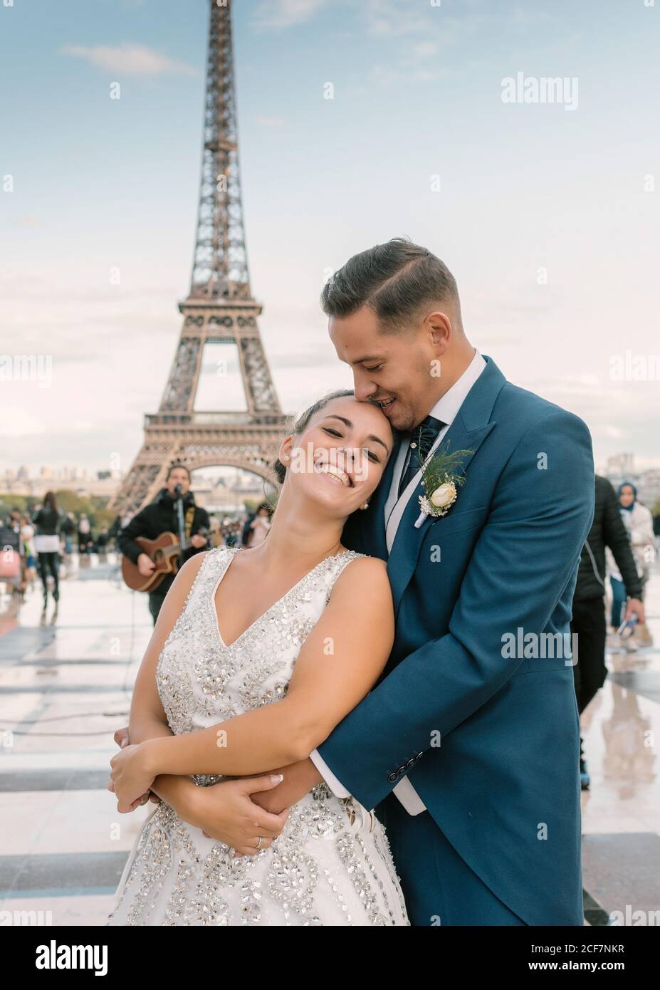 Sposo in abito da sposa blu in abito da sposa bianco Coccolarsi e sorridere con la Torre Eiffel sullo sfondo a Parigi Foto Stock