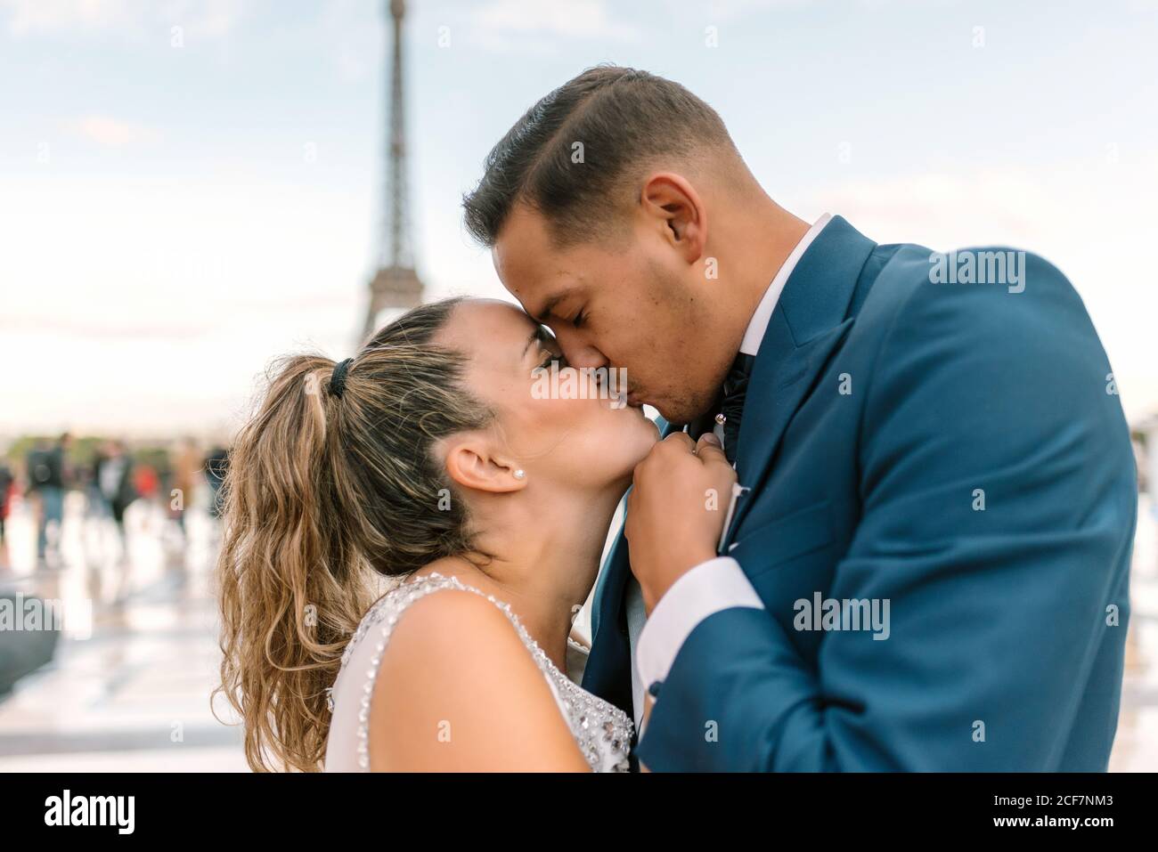 Sposo in abito da sposa blu in abito da sposa bianco Baciando con passione con la Torre Eiffel sullo sfondo a Parigi Foto Stock