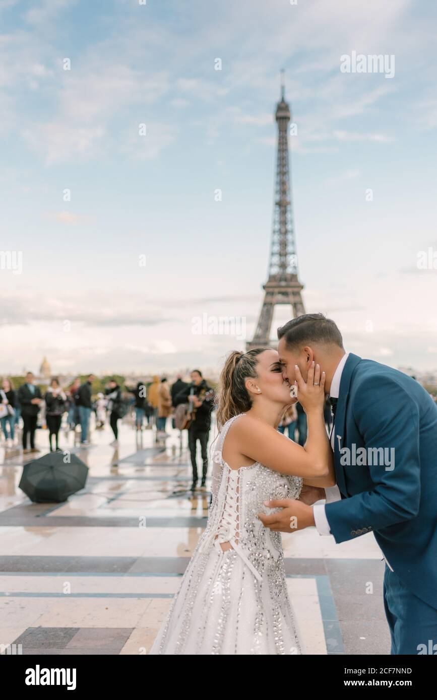 Sposo in abito blu inginocchiato e sposa in matrimonio bianco Gown baciare appassionatamente con la Torre Eiffel sullo sfondo a Parigi Foto Stock