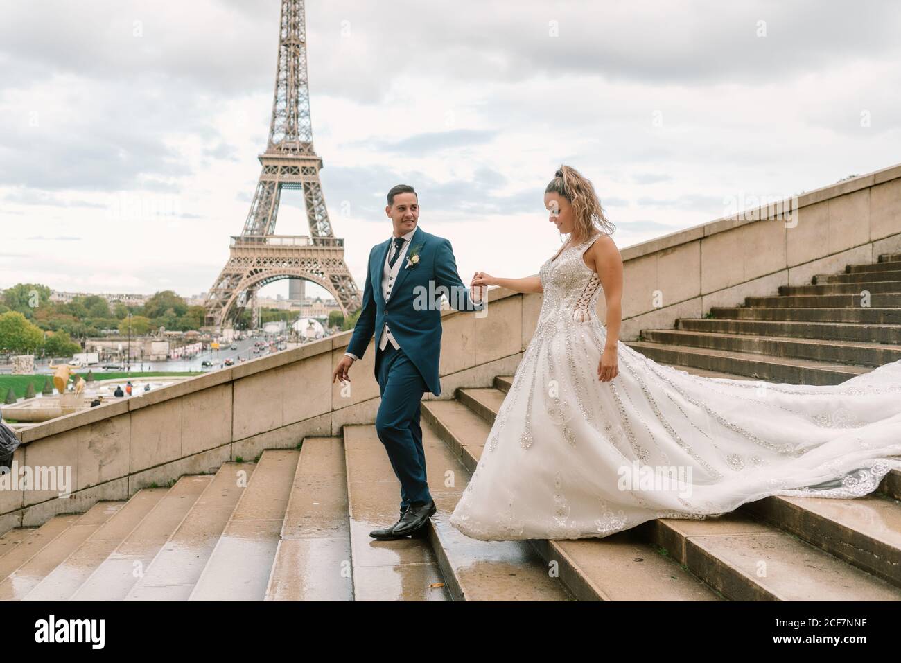 Sposo in sposa guida con tuta blu in abito da sposa bianco Al piano inferiore con la Torre Eiffel sullo sfondo a Parigi Foto Stock