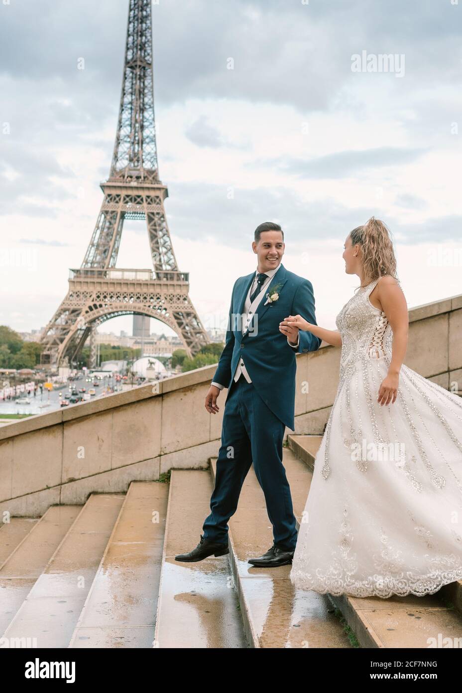 Sposo in sposa guida con tuta blu in abito da sposa bianco Al piano inferiore con la Torre Eiffel sullo sfondo a Parigi Foto Stock