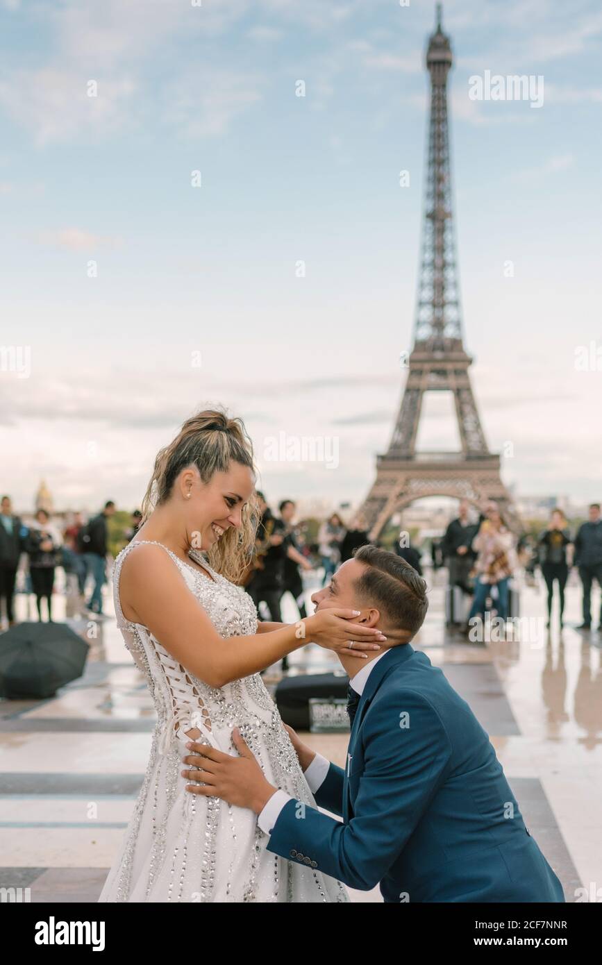Sposo in abito blu inginocchiato e sposa in matrimonio bianco Coccolati con la Torre Eiffel sullo sfondo di Parigi Foto Stock