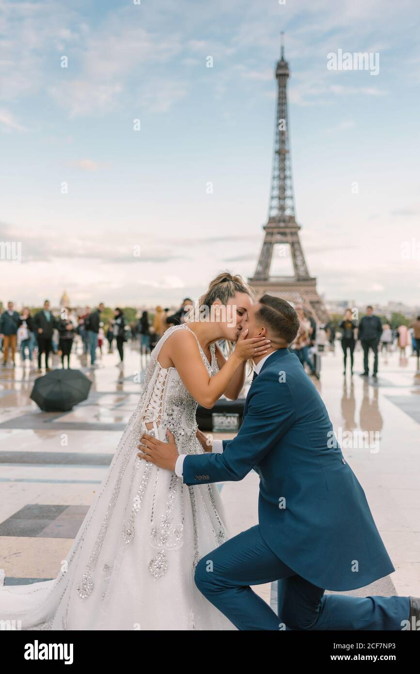 Sposo in abito blu inginocchiato e sposa in matrimonio bianco Gown baciare appassionatamente con la Torre Eiffel sullo sfondo a Parigi Foto Stock