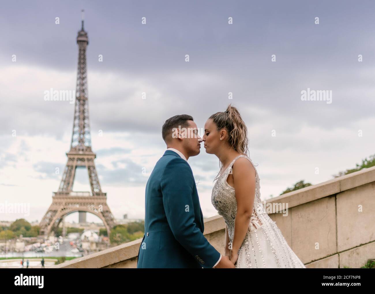 Sposo in abito da sposa blu in abito da sposa bianco Baciando con passione con la Torre Eiffel sullo sfondo a Parigi Foto Stock