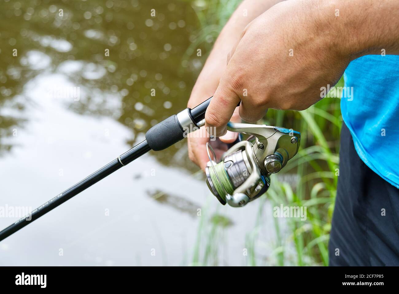 mano del pescatore con filatura e bobina sul lago d'estate, primo piano. Foto Stock