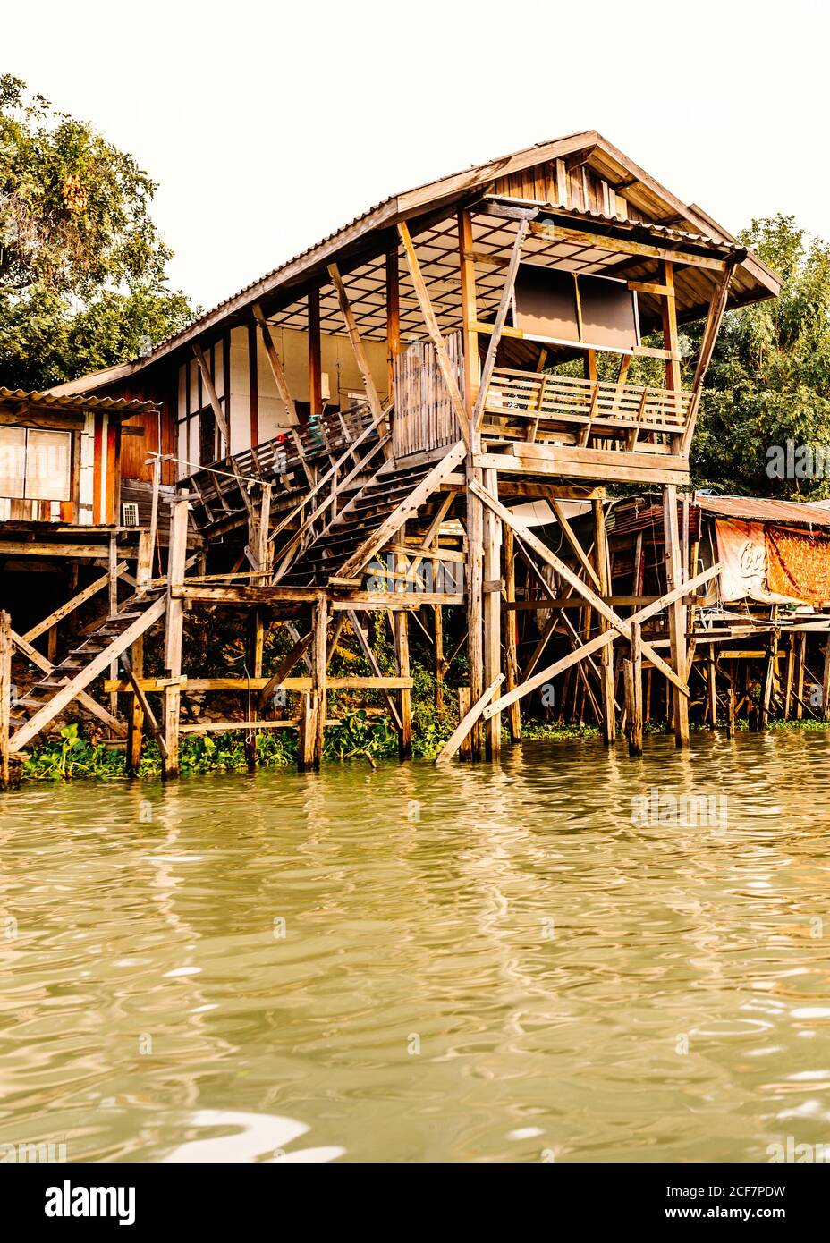 Grande casa di legno su palafitte con scale situate sulla riva di lago tra piante verdi Foto Stock