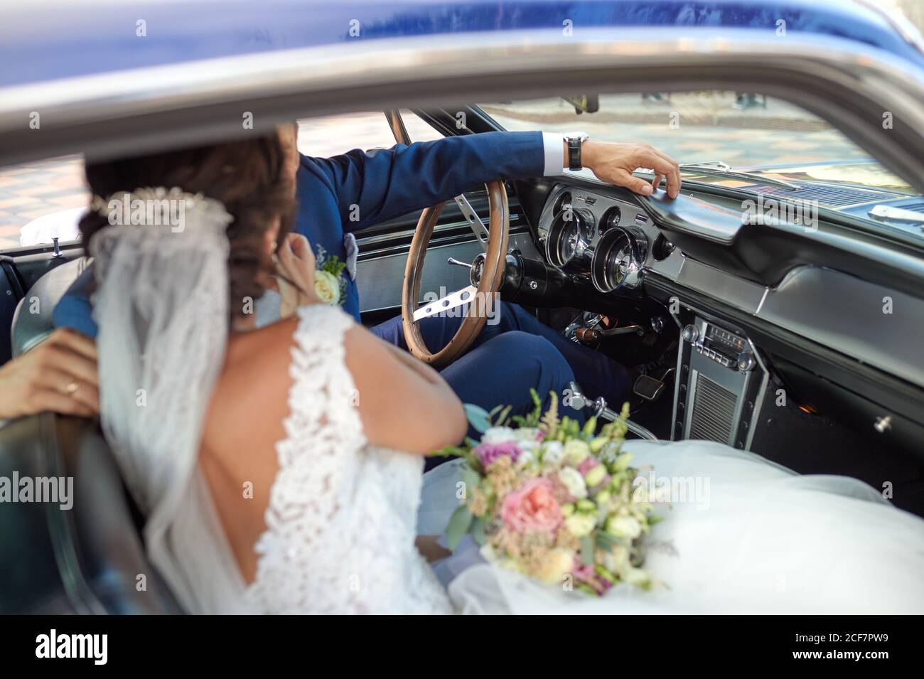 Sposa felice in abito da sposa e sposo in abito di classe seduto in un'automobile d'epoca e guardandosi l'un l'altro Foto Stock