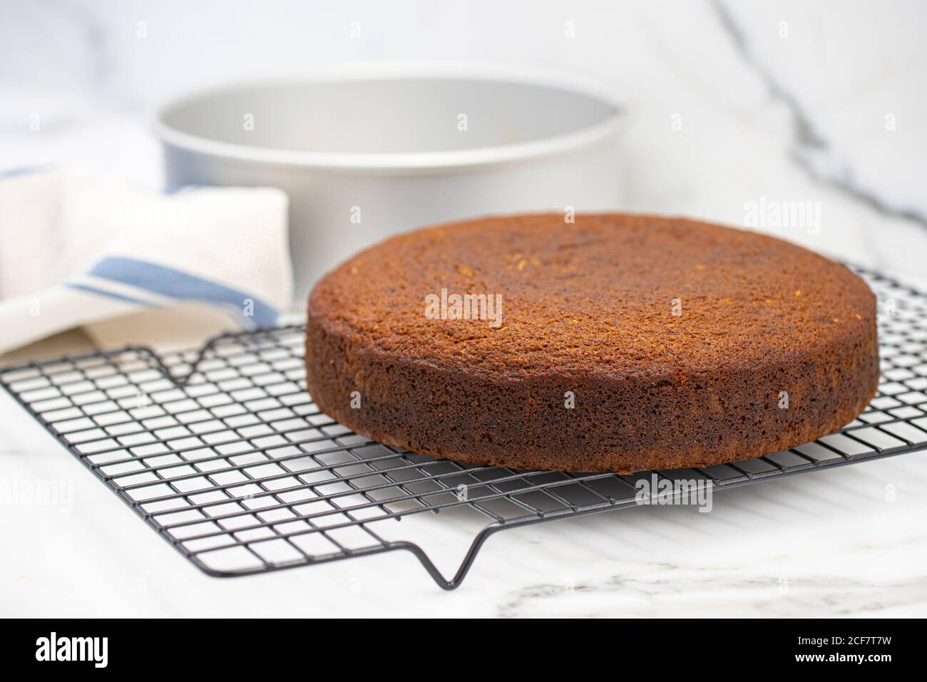 Raffreddamento della torta appena sfornata su griglia metallica con padella per torte in background Foto Stock