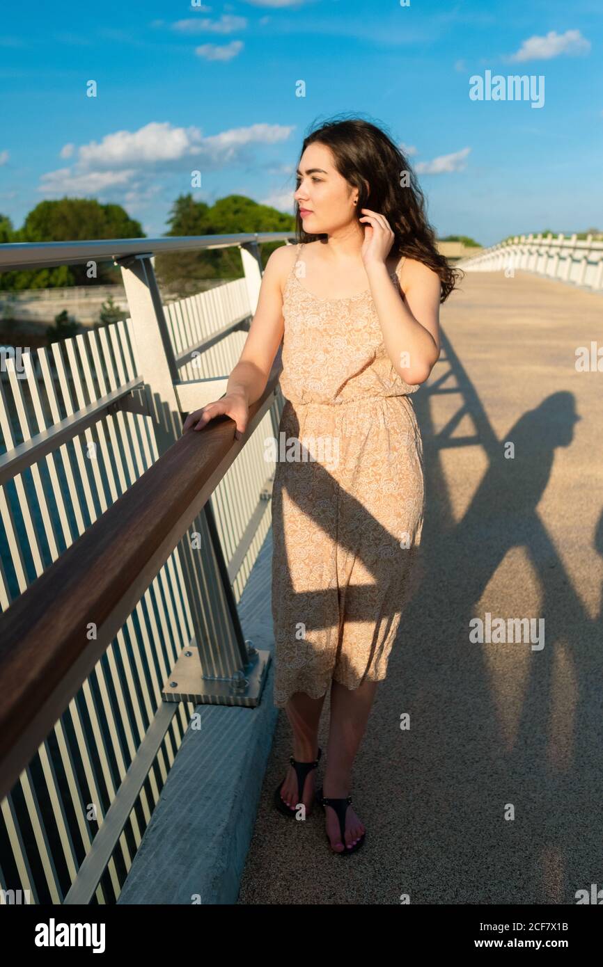 Rilassato Donna in sundress passeggiando lungo il ponte in sole giornate ventose Foto Stock