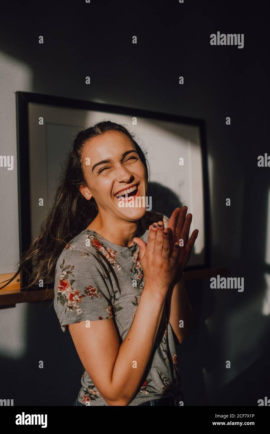 Uscito casual giovane donna in t-shirt ridendo e battendo le mani mentre si è in piedi accanto a parete bianca Foto Stock