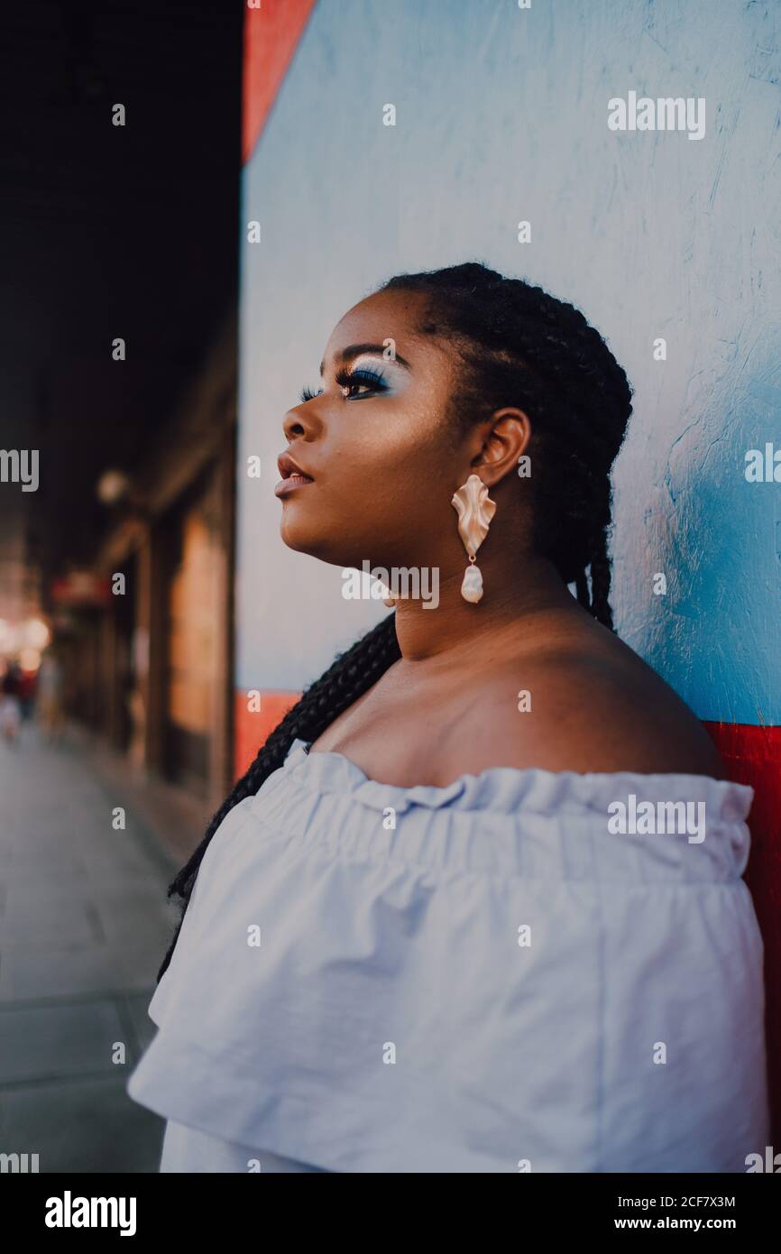 Giovane donna giovane e moderna, moderna e giovane donna nera, con un brillante make-up in un abito a spalle scoperte che guarda lontano Foto Stock