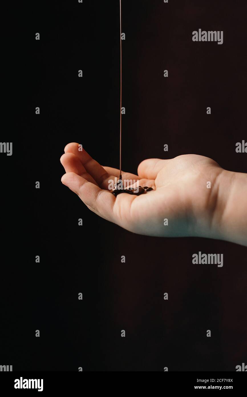 Appetitoso cioccolato caldo fuso che viene versato su una persona non riconoscibile tagliata mano posta su sfondo scuro Foto Stock